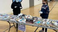2 kids standing next to tables with books