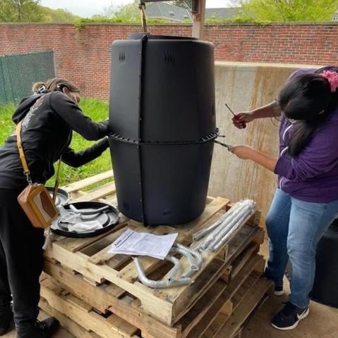 Composting Bin 2 students are building a compost bin . They are each using a screwdriver to attach the two sections of the barrels together.