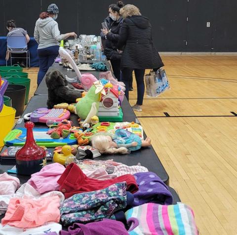Tables with children clothing and toys at the Stop and Swap event 2 people standing next to tables with children clothing and toys